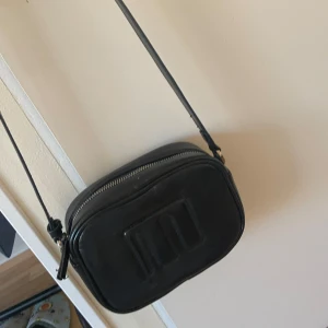 Svart axelremsväska med m logga från mango🤍 - Snygg svart axelremsväska i skinn. Väskan har en justerbar axelrem och en dragkedja upptill. Framsidan är lite skrynklig eftersom den är köpt för ett tag sen🤍Nypriset var 600kr🤍Jag säljer den för 170kr eftersom den är använd❗️