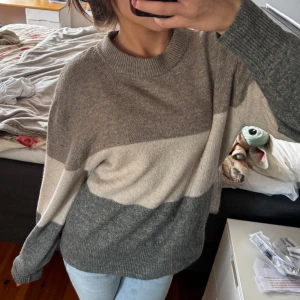 Randig stickad tröja i grå toner - Supermysig stickad tröja med breda ränder i olika grå nyanser och beige. Tröjan har rund halsringning, lång ärm och relaxed fit. Perfekt för dig som gillar en chill och stilren look till höst och vinter.