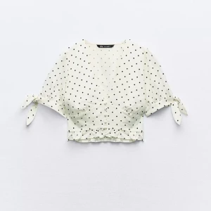 Prickig croppad blus från Zara - Superfin vit croppad blus med svarta prickar från Zara. Blusen har korta ärmar med knyt i sidan, v-ringning och volangdetalj längst ner. Så himla söt och perfekt till sommaren🙌🏽🙌🏽 Använd vid två tillfällen endast!