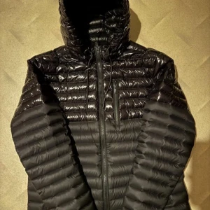 Svart pufferjacka Moose Knuckles - Säljer en svart pufferjacka från Moose Knuckles med glansig finish och huva. Jackan har dragkedja framtill, bröstficka med dragkedja och ikonisk logga på ärmen. Perfekt för kalla dagar och riktigt snygg streetstil.