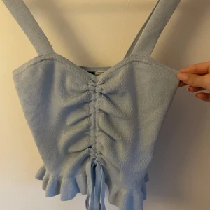 Ljusblå stickad linnetopp H&M - Supersöt ljusblå stickad linnetopp från H&M Divided. Toppen har breda axelband, rynkade detaljer med snörning framtill och volangkant nertill. Perfekt för en trendig och somrig look!