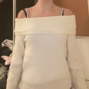 Vit offshoulder stickad tröja - Superfin vit stickad tröja med bred offshoulder-ringning. Tröjan är ribbstickad och har långa ärmar, perfekt för dig som gillar en stilren och trendig look. Snygg att styla med jeans eller kjol för en chill vibe.