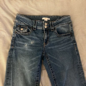 Blå jeans från Gina Tricot - Snygga blå low waist jeans från Gina Tricot Young med klassisk ficksdesign och dubbla knappar i midjan. Jeansen har kontrastsömmar, lätt slitning framtill och en liten ficka med lock. Har pälsdjur hemma, kontakta mig vid intresse!