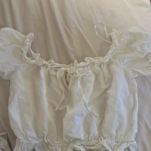Vit puffig topp med rosett - Supersöt vit topp med puffiga ärmar. Toppen har en rosett framtill och resår vid både halsringning och midja. Använd enstaka gång💕 Storlekslappen är däremot av men den är S men resårbanden kan göra att den får plats i en M men isåfall blir den croppad!❤️