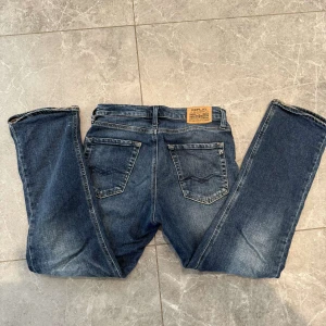 Blå Replay jeans straight fit - Snygga blå jeans från Replay med klassisk femficksdesign och raka ben. Jeansen har en mörk tvätt med lätt slitning och tydliga sömmar. Märkespatch bak i midjan och diskret logga på bakfickan. Perfekta för en avslappnad och stilren look.