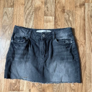 Svart jeanskjol med rå kant - Cool jeanskjol med rå, fransig kant nertill. Klassisk femficksmodell med bälteshällor och knappstängning. Perfekt för dig som gillar en avslappnad och edgy stil.