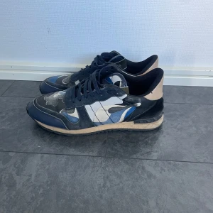 Valentino Garavani Rockrunners  - Snygga sneakers från Valentino Garavani med blå, svarta och vita camouflage-detaljer. Skorna har snörning, platt sula och rund tå. Tillverkade i en mix av skinn och textil för en lyxig känsla. Perfekta för dig som vill sticka ut med en unik design.