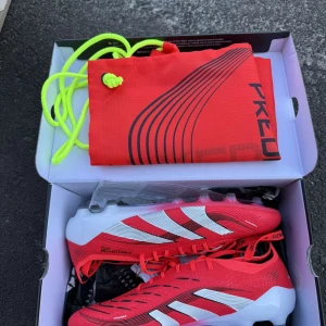 Adidas predator elite fold-over tongue  - Snygga röda Adidas Predator fotbollsskor med vita och svarta detaljer. Skorna har snörning och är tillverkade i syntetmaterial för bästa grepp och känsla på planen. Perfekta för dig som vill sticka ut med stil och prestanda. Skorna är även helt oanvända! Nypris 3299kr
