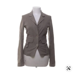 Beige kavaj från VILA i linneblandning - Snygg beige kavaj från VILA med två knappar framtill och fickdetaljer med lock. Figursydd modell i mjuk linneblandning som ger en chill men dressad vibe. Perfekt till jeans eller kjol när du vill steppa upp din outfit.