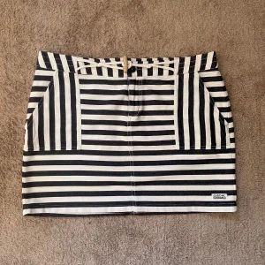 Randig kortkjol från Dobber - Snygg kortkjol från Dobber med svartvita ränder i olika riktningar. Kjolen har två stora fickor fram och bälteshällor i midjan. Perfekt för dig som gillar en cool och stilren look med lite edge.