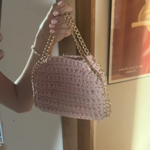 Rosa virkad handväska med guldkedja - Superfin handväska i ljusrosa virkat tyg med chunky guldfärgad kedja som axelrem. Väskan har magnetlås och en mjuk, boxig form. Perfekt för dig som vill ha en söt och trendig accessoar som sticker ut. Liknar en Stella! Falabella storlek på pricken!