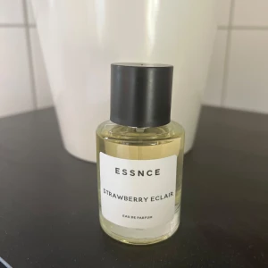 ESSNCE Strawberry Eclair parfym - ESSNCE Strawberry Eclair Eau de Parfum har en söt och gourmand doft med toner av jordgubbar, vanilj och bakverk. Flaskan är rund i genomskinligt glas med svart lock och vit etikett. Perfekt för dig som gillar fruktiga och dessertinspirerade parfymer. Endast testad . 