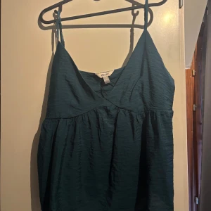 Mörkgrön linnetopp från AWARE ( Vero Moda ) - Supersöt mörkgrön linnetopp från AWARE med tunna axelband och v-ringning. Toppen har en luftig och flowy passform med lätt rynkade detaljer under bysten. Perfekt för varma dagar och enkel att styla med jeans eller kjol. Använd endast en gång så bra skick👐🫶🏻