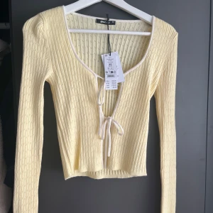 Ljusgul ribbad topp från Gina Tricot - Supersöt ljusgul ribbad topp från Gina Tricot med lång ärm och croppad passform. Djup v-ringning med knyt framtill och vita kanter som ger en extra detalj. Storlek XS, helt ny! Prislapp kvar ☀️💕