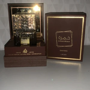 Lattafa Khamrah Qahwa  - Lattafa Khamrah Qahwa Eau de Parfum 100ml i lyxig brun och guldig förpackning. Flaskan har ett elegant rutmönster och guldiga detaljer, och boxen är robust med guldfolierade kanter. Perfekt för dig som gillar exklusiva dofter och snygg design. 80ml/100ml