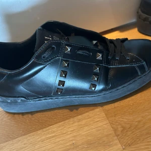 Valentino Rockstud svarta sneakers - Svarta Valentino Rockstud sneakers i skinn med ikoniska nitar längs sidorna och tungan. Klassisk rund tå, svarta snören och platt sula. Skorna har avier använda men är i fint skick. Kontakta gärna vid frågor.