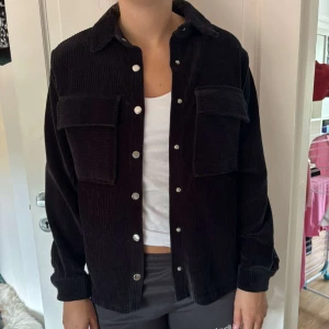 Svart manchester overshirt - Svart overshirt i manchester från Black Story. Jackan har klassisk krage, stora bröstfickor med lock och silverfärgade knappar framtill. Långärmad och loose fit, perfekt att slänga över en t-shirt för en chill look.