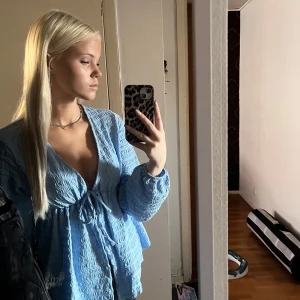 Ljusblå omlottblus med knyt - Supersöt ljusblå blus med omlottkänsla och knyt framtill. Blusen har lång ärm, v-ringning och ett vågigt, strukturerat tyg som ger en unik look. Perfekt för dig som gillar trendiga och feminina detaljer.använd en gång 