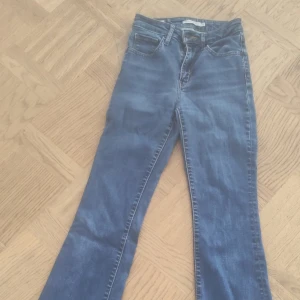 Levi's 725  blå high rise bootcut jeans - Säljer ett par klassiska blå Levi's jeans i bootcut-modell med hög midja. Jeansen har fem fickor, snygga sömmar och är tillverkade i slitstarkt denim. Perfekta för dig som gillar en tidlös och avslappnad stil.