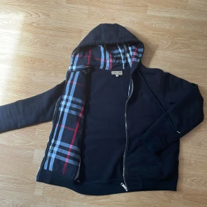 Svart ziphoodie från Burberry M - En fet svart burberry hoodie som är i storlek M men den är liten i storleken så den passar storlek S, de är fett nice material och skön o ha på sig.  Använd ett fåtal gånger, Kan gå ner i pris vid snabbt köp 