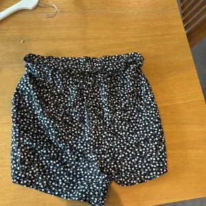 Svarta blommiga shorts från Monki - Snygga svarta shorts från Monki med ett gulligt blommigt mönster i rosa och vitt. De har elastisk midja och perfekta för varma dagar. Passformen är loose och de är superbekväma att bära.❣️❣️❣️ Strl M!!❣️❣️