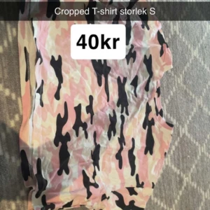 Cropped camo t-shirt rosa S - Cropped t-shirt i camouflagemönster med rosa, beige och svarta toner. Kortärmad och loose fit, perfekt för en chill och trendig look. Mjuk och skön, passar till allt.