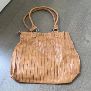 Vintage❤️Beige axelväska i skinnimitation - Stor beige axelväska med två rejäla handtag och vertikala sömmar som ger en cool struktur. Väskan har dragkedja upptill och rymligt innerfack med extra ficka. Perfekt för dig som vill ha plats för allt du behöver under dagen.