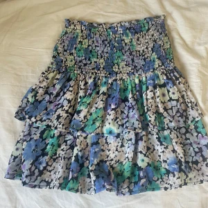 Blommig volangkjol från Kappahl XS - Knappt använd i nyskick. Storlek XS men passar upp till M då den är mycket strechig. Supersöt kort volangkjol från Kappahl i blommigt mönster med blå, gröna, lila och svarta toner. Kjolen har smock i midjan och flera lager volanger som ger en flowy känsla. Perfekt för vår och sommar! 