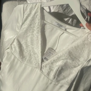 Vit spetsklänning från NA-KD - Superfin oanvänd vit klänning från NA-KD med v-ringning och spetsdetaljer upptill. Långärmad modell i mjukt satin som känns lyxigt och stilrent. Perfekt för dig som vill ha en fin midsommar- eller festklänning💕