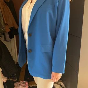 Blå kavaj från Vero Moda - Säljer en helt ny oanvänd elegant blå kavaj från Vero Moda med klassisk krage och två knappar framtill. Axlarna är vadderade. Den är stor i storleken. Den första bilden är på min mamma som typ brukar ha 42, så den är väldigt oversized. (⚡️Nypris 449kr⚡️) Skriv vid frågor❤️❤️