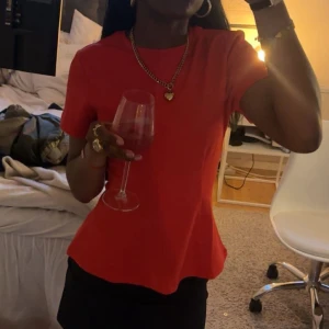 Röd kortärmad topp i figurnära modell - Snygg röd topp med rund hals och korta ärmar. Modellen är figurnära och enkel, perfekt att styla med smycken eller kjol. Tidlös design som passar till många olika looks.