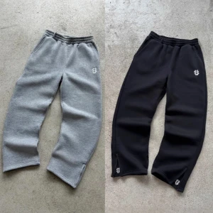 Gråa och svarta mjukisbyxor med brodyr - Två par mjukisbyxor i grått och svart med elastisk midja och broderad logga på vänster lår, dem är ej använda och kommer i storlekar s,m,l,xl 