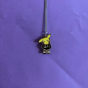 Halsband med Pikachu-hänge - Snyggt halsband med ett Pikachu-hänge i silverfärg. Hänget föreställer Pikachu i svart outfit med gula detaljer och röda kinder. Perfekt accessoar för dig som älskar Pokémon och vill sticka ut med något unikt.