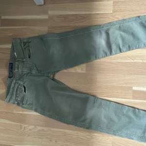 Replay Grover gröna jeansbyxor - Snygga Replay Grover jeansbyxor i en dov grön färg. Klassisk femficksmodell med raka ben och diskreta röda detaljer vid fickorna. Tillverkade i mjuk bomull med en skön passform som funkar till många olika stilar. 30/30