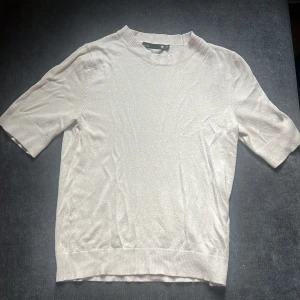 Ljusbeige stickad tröja 157 XS - En stilren ljusbeige stickad tröja från 157 i storlek XS. Tröjan har korta ärmar, ribbade muddar och en klassisk rund halsringning. Perfekt för lager-på-lager och funkar året runt. Enkel att matcha med både jeans och kjol.