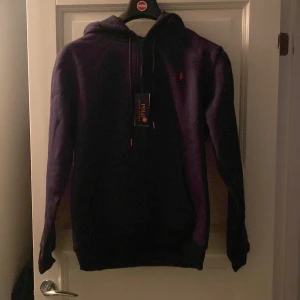 Marinblå hoodie från Polo Ralph Lauren - Säljer en marinblå hoodie från Polo Ralph Lauren med klassisk huva och dragsko. Tröjan har en liten röd logga broderad på bröstet och är tillverkad i mjuk bomull. Perfekt för dig som gillar en avslappnad och stilren look. 