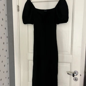 Svart långklänning med puffärm - Supersnygg svart långklänning från Gina Tricot med puffiga kortärmar och snörning framtill vid bysten. Klänningen har en figurnära passform och är gjord i mjuk bomull, perfekt för dig som gillar en stilren och trendig look. Nästan aldrig använt