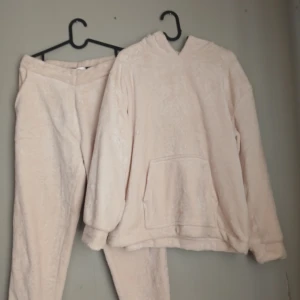 Creamfärgade fleecehoodie + byxor från Kappahl stl M - Supermjuk och fluffig cremefärgad hoodie och byxor ifrån Kappahl i fleece- lite ljusare än på bild. Tröjan har huva, lång ärm och en stor magficka framtill. Perfekt för dig som gillar oversized och mysiga vibes. Passar till chill hemma eller när du vill vara extra bekväm.