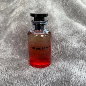 Louis Vuitton On The Beach  - Exklusiv parfym från Louis Vuitton, On The Beach, i en snygg glasflaska med röd-orange gradient och svart lock med LV-logga. Flaskan rymmer 100 ml Eau de Parfum och kommer i originalförpackning med matchande färgskala. Perfekt för dig som gillar lyxiga dofter. Priset är förhandlingsbart. 