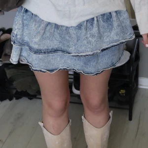 Blå jeanskjol med volanger - Supersöt kort jeanskjol i ljusblå tvätt med två volanglager och råa kanter. 