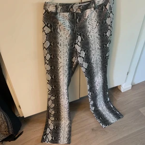 Ormmönstrade skinnbyxor I.AM.GIA - Säljer ett par riktigt snygga skinnbyxor från I.AM.GIA i storlek L. Byxorna har ett grått och svart ormmönster, dragkedja framtill och går att föra igenom ett snöre utanpå byxorna
