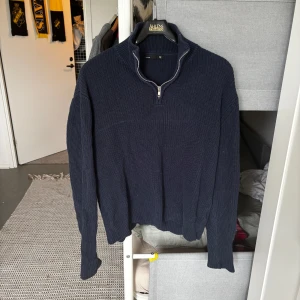 Mörkblå stickad half zip-tröja - Mörkblå stickad tröja med half zip och hög krage. Tröjan har lång ärm och är ribbstickad för en schysst struktur. Perfekt för lager-på-lager och chillare dagar.