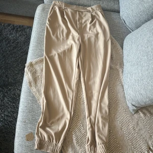 Beiga mjukisbyxor med resår, stl M - Köpte precis säkert sett reklamen på Facebook med kvinna solbränd med vit skjorta, jättesnygga men passar inte till min mage, det är som ”finbyxor”. Beiga mjukisbyxor i 100% polyester med resår i midjan och vid bensluten. Byxorna har en avslappnad passform och är perfekta för en chill och bekväm stil. Snyggt enkla utan mönster eller detaljer, passar till allt.