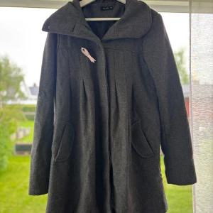 Mörkgrå kappa från Vila i ullmix - Snygg mörkgrå kappa från Vila i ullmix med bred krage och fina veckdetaljer både fram och bak. Jackan har två fickor och stängs framtill. Perfekt för dig som vill ha en stilren och klassisk look under höst och vinter.