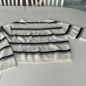 Randig stickad tröja från H&M - Vit och svart randig stickad tröja från H&M i storlek 146/152. Tröjan har en klassisk rund halsringning och långa ärmar. Den ribbade strukturen ger en snygg och avslappnad look, perfekt för dig som gillar stilrena basplagg med lite edge.