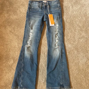 Blå bootcut jeans Gina Tricot 140 - Snygga ljusblå bootcut jeans från Gina Tricot i storlek 140. Jeansen har slitna detaljer framtill, klassiska fickor och markerade sömmar. Tillverkade i jeansmaterial med cool tvätt och knäppning fram.
