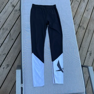 Svarta och vita träningsleggings SOC - Snygga svarta leggings från SOC med vita partier nedtill och en stor logga på ena benet. Tillverkade i ett tekniskt material som andas och håller dig torr under träning. Perfekta för dig som vill ha en sportig och stilren look.