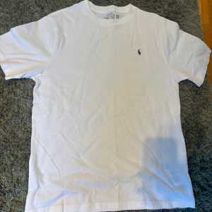 Vit t-shirt från Polo Ralph Lauren - Klassisk vit t-shirt från Polo Ralph Lauren med rund hals och ikoniska broderade loggan på bröstet. Tillverkad i mjuk bomull och har en normal passform. Perfekt basic-plagg med stilren look. Riktigt najs tröja aldrig använda bara legat i gaderoben.