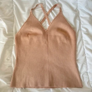 Beige ribbad linnetopp med korsade band - Supersnygg beige ribbad linnetopp med smala axelband som korsas i ryggen. Toppen har v-ringning och är figurnära med stretchigt material. Perfekt för varma dagar eller lager på lager. Enkel men trendig design som passar till allt