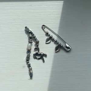 Silvriga nyckelringar med pärlor och föl - Unika silvriga pärldetaljer och berlocker. Ena har en hästberlock och små pärlor i silver och vitt, det andra är en säkerhetsnål med silverfärgade löv. Perfekt för dig som gillar statement-smycken med coola detaljer.